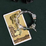 Beaded bracelet with clear beads, green stone beads, and silver sword drop