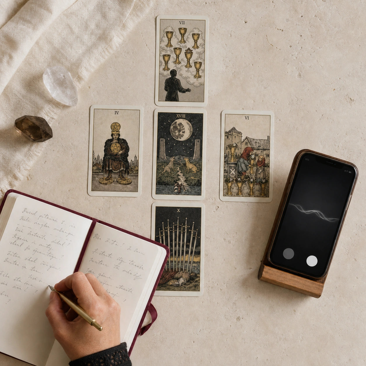 Tarot card spread with a hand writing in a notebook beside a phone
